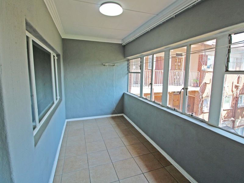 An enclosed balcony featuring tiled flooring, large windows, and a wall-mounted drying rack, offering a versatile space for laundry or relaxation.