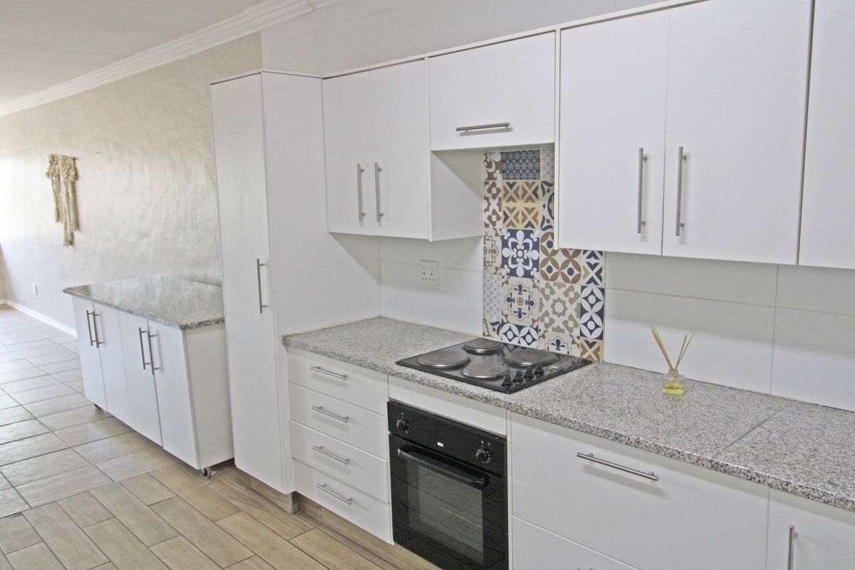 Modern kitchen featuring white cabinetry, granite countertops, a built-in oven, electric hob, and decorative tiled splashback, set against neutral tiled flooring.
