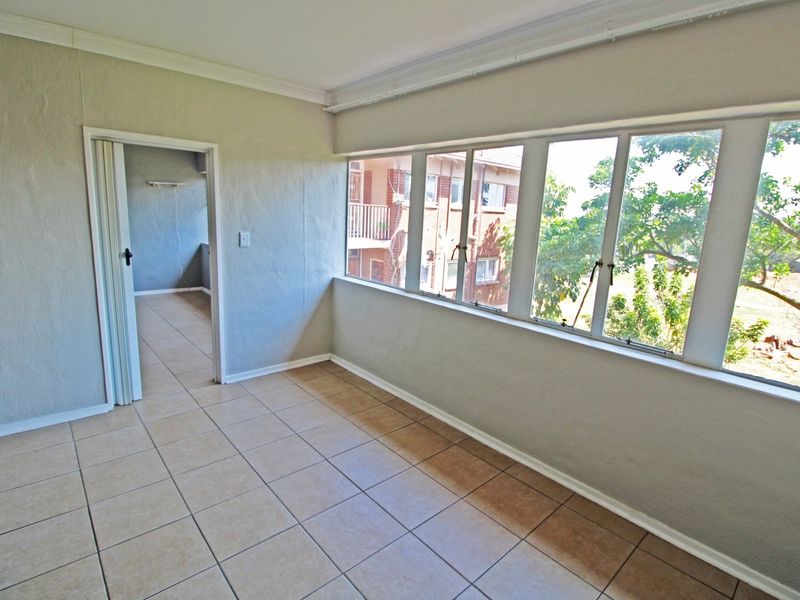 An empty, enclosed balcony or sunroom featuring tiled flooring and a large bank of windows providing natural light and exterior views.