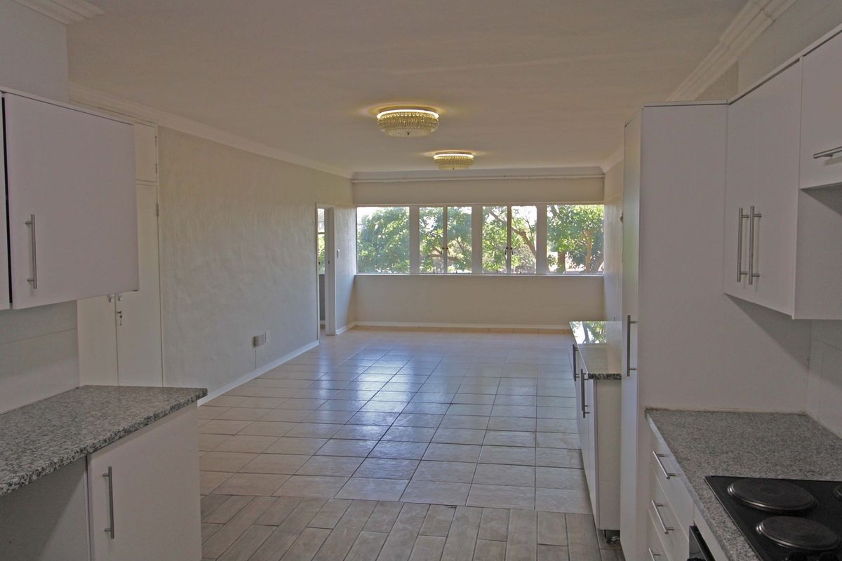 Spacious open-plan living and kitchen area featuring tiled flooring, modern white cabinetry with granite countertops, and large windows providing natural light.