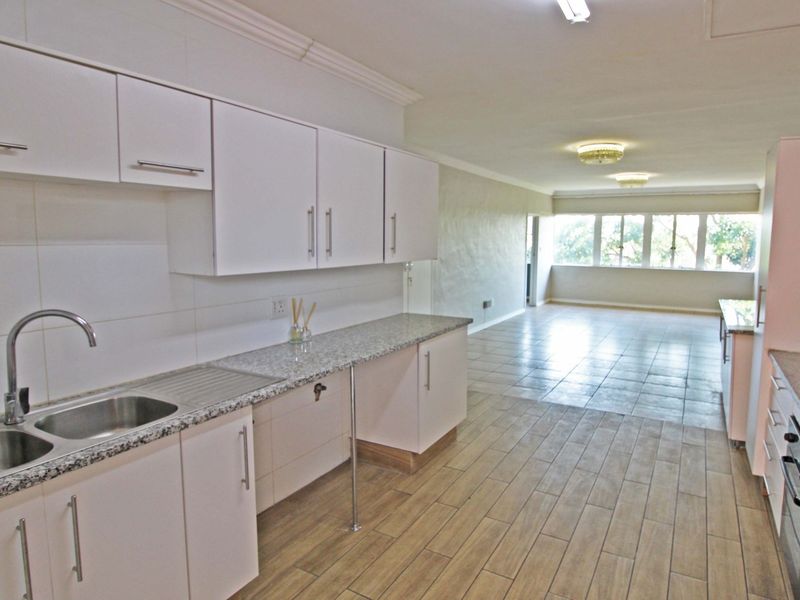 Spacious open-plan kitchen and living area featuring modern white cabinetry, granite countertops, built-in oven, hob, and large windows providing ample natural light.