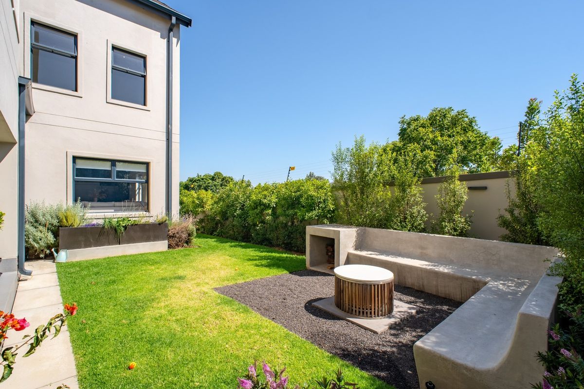A well-maintained rear garden featuring a built-in concrete bench and fire pit area, complemented by lush landscaping and a private boundary wall.