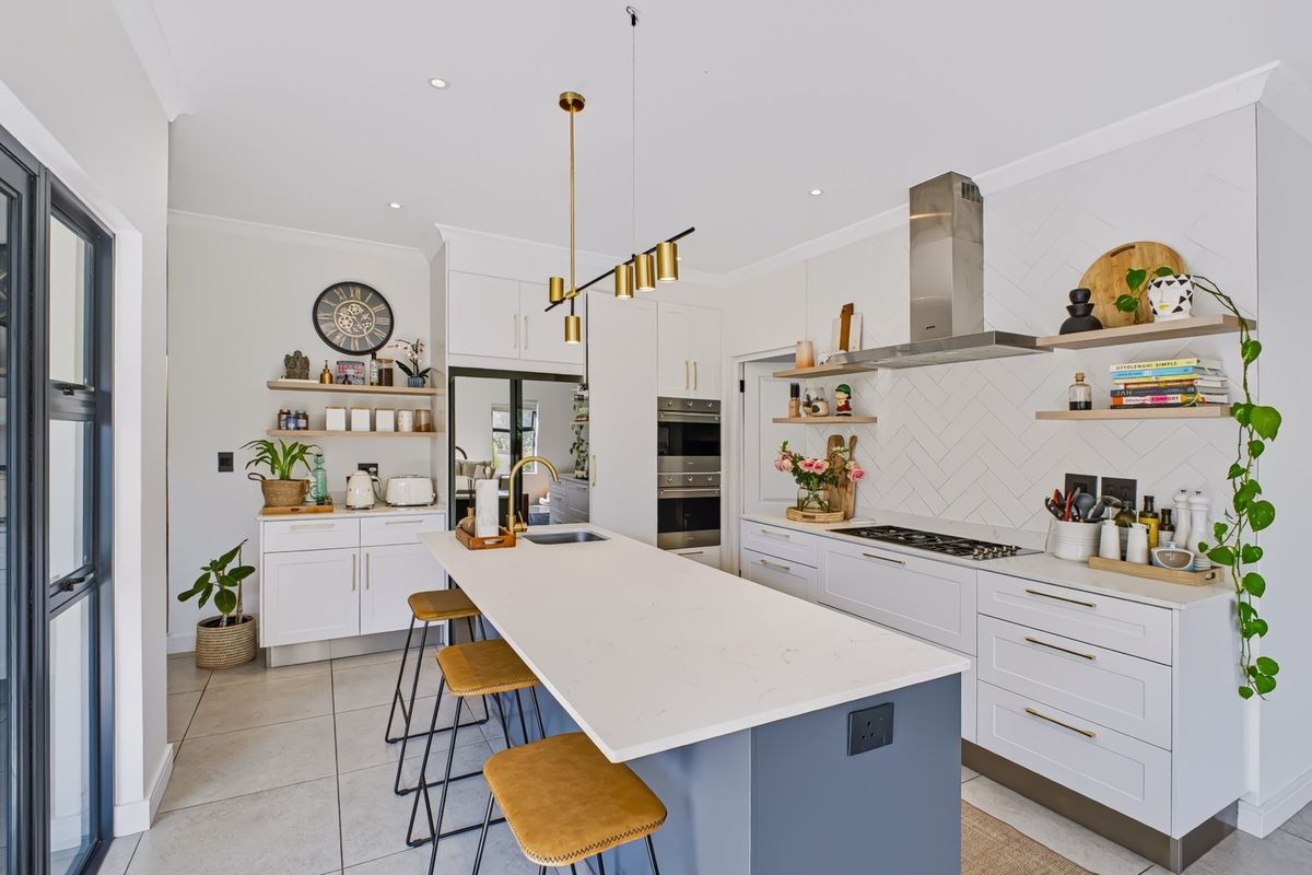 Modern kitchen featuring a central island with stone countertops, herringbone backsplash, built-in appliances, and stylish pendant lighting in a bright, open-plan layout.