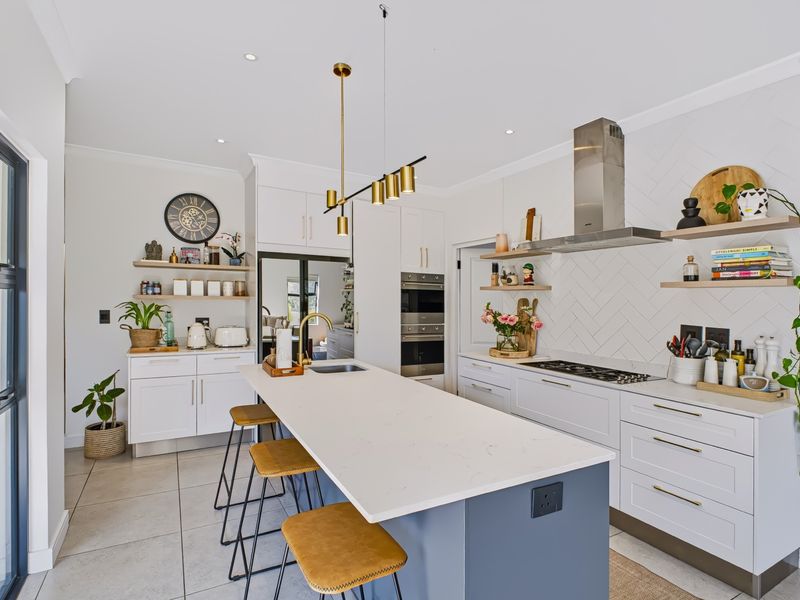 Modern kitchen featuring a central island with stone countertops, herringbone backsplash, built-in appliances, and stylish pendant lighting in a bright, open-plan layout.