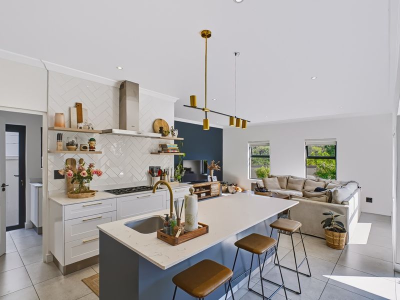 Modern open-plan living area featuring a sleek kitchen with a central island, herringbone backsplash, and integrated gas cooktop, flowing into a comfortable lounge space.