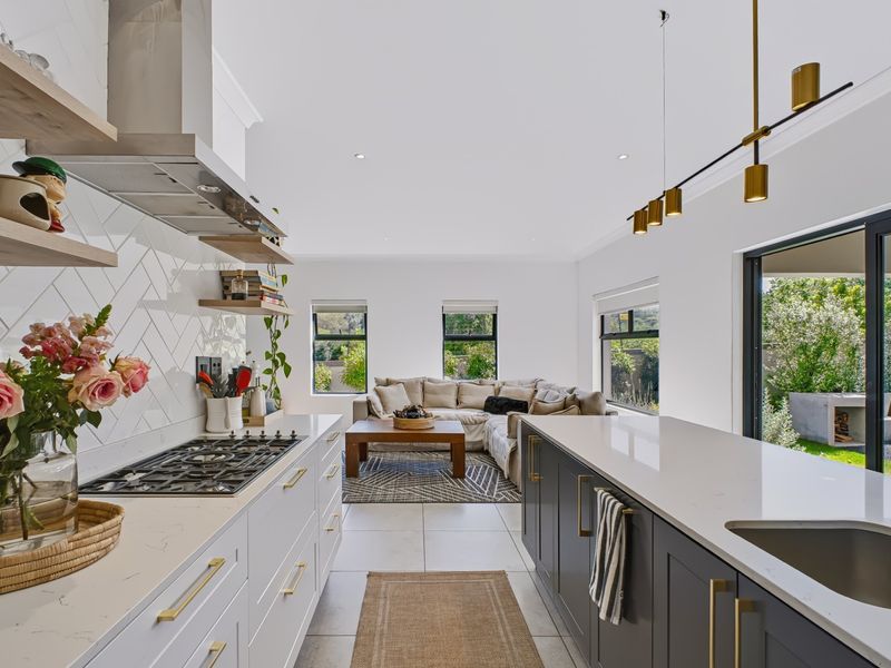 Modern open-plan kitchen and living area featuring quartz countertops, shaker cabinetry, herringbone backsplash, and seamless access to the outdoor patio through sliding glass doors.