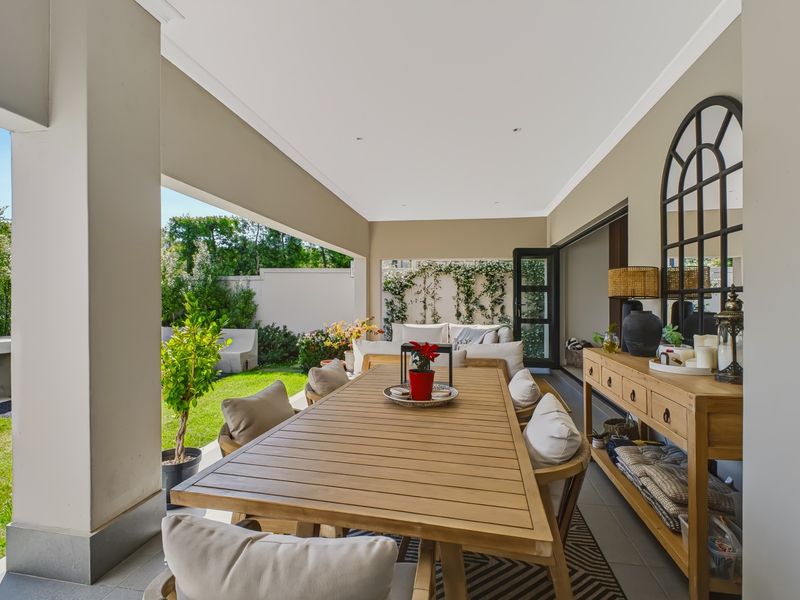 A spacious covered patio featuring tiled flooring, recessed lighting, and a built-in outdoor fireplace, seamlessly connecting to the garden and interior living space.