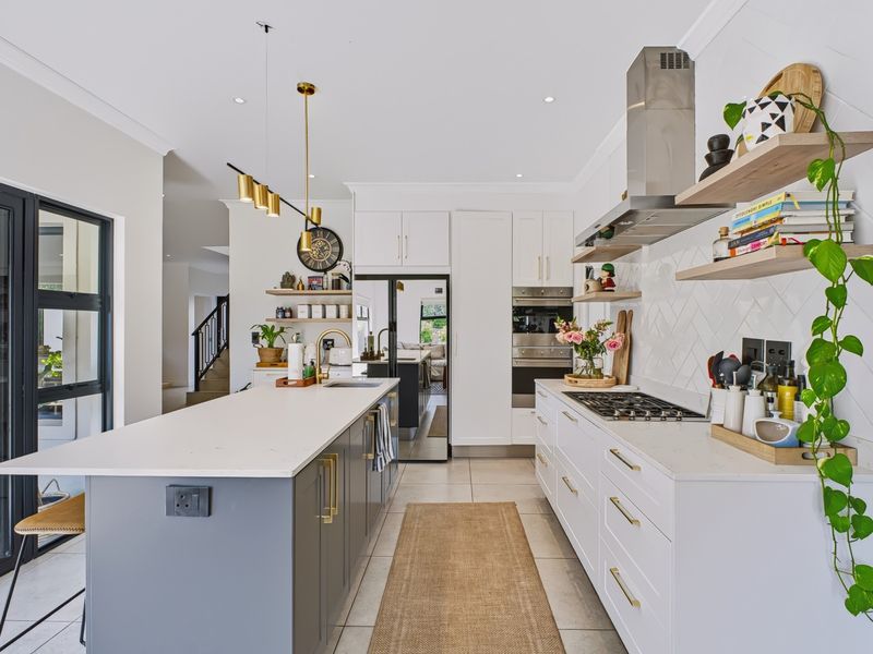 Modern kitchen featuring a central island with stone countertops, shaker cabinetry, herringbone backsplash, built-in appliances, and elegant pendant lighting.