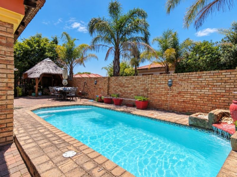 A well-maintained outdoor pool area featuring a brick-paved surround, a decorative water feature, and a charming thatched gazebo in the garden.