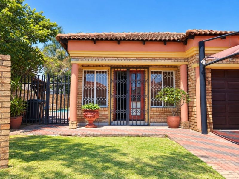 A well-maintained rear exterior view featuring a face brick facade, tiled roof, paved patio area, and secure metal fencing.