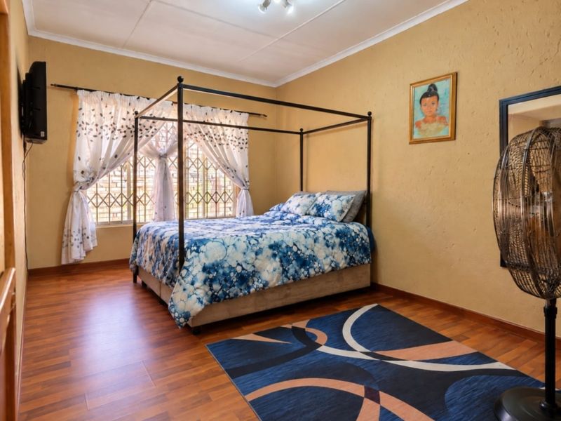 A well-proportioned bedroom featuring warm-toned laminate flooring, textured walls, and security bars on the windows.