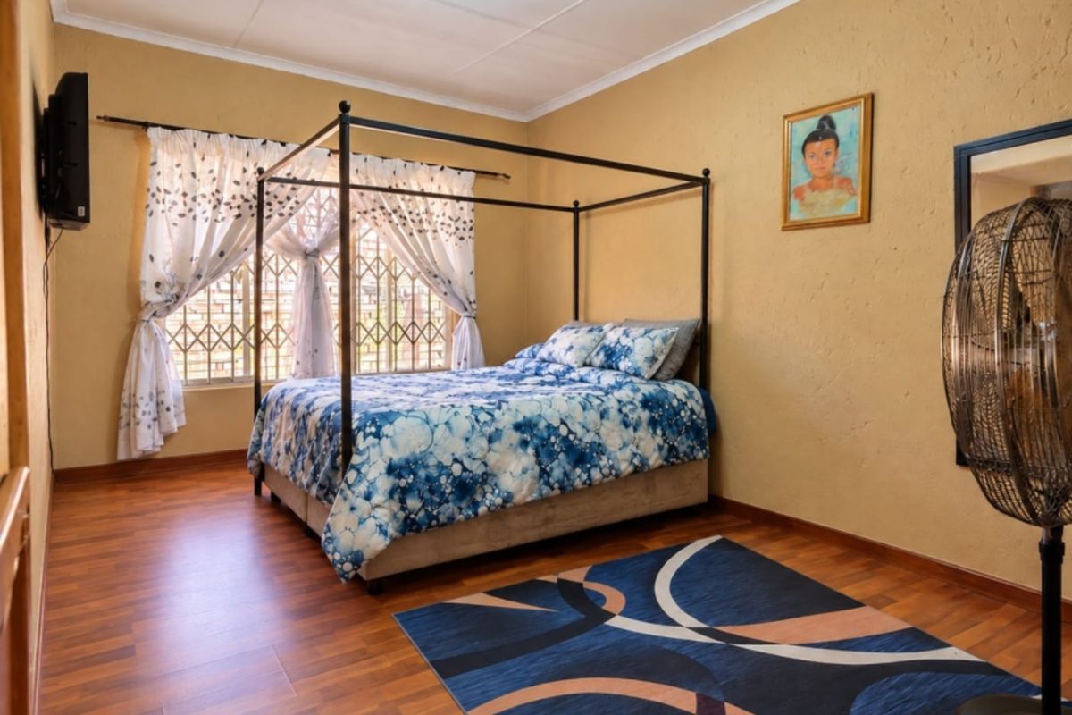 A well-proportioned bedroom featuring warm-toned laminate flooring, textured walls, and security bars on the windows.