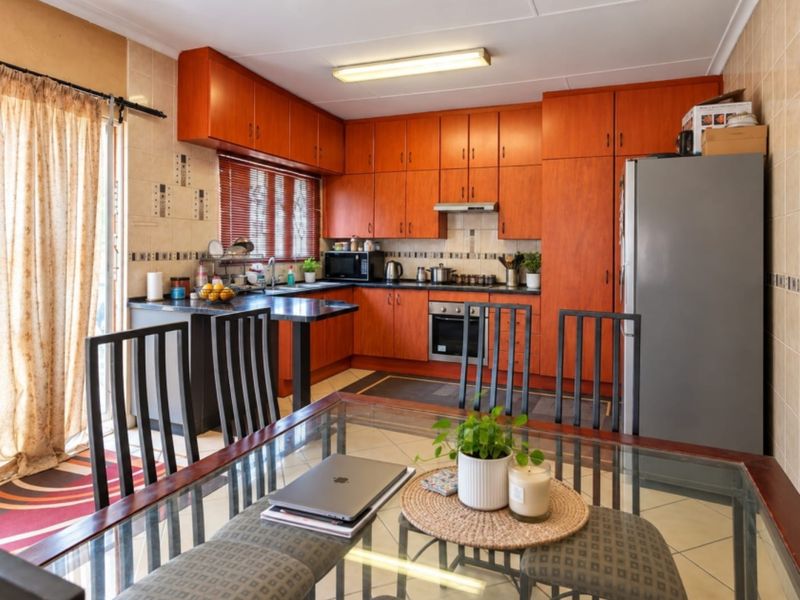 Open-plan kitchen and dining area featuring warm-toned built-in cabinetry, tiled flooring, and direct access to the outdoor space via a sliding door.