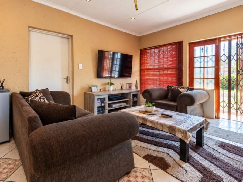 A comfortable living room featuring tiled flooring, recessed lighting, and direct access to the exterior through a secure timber-framed glass door.
