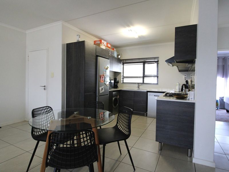 Open-plan kitchen and dining area featuring modern dark cabinetry, tiled flooring, and integrated appliances, creating a functional and contemporary living space.