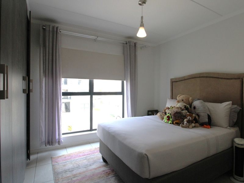 A well-maintained bedroom featuring tiled flooring, a built-in wardrobe, and large aluminium-framed windows that provide natural light.