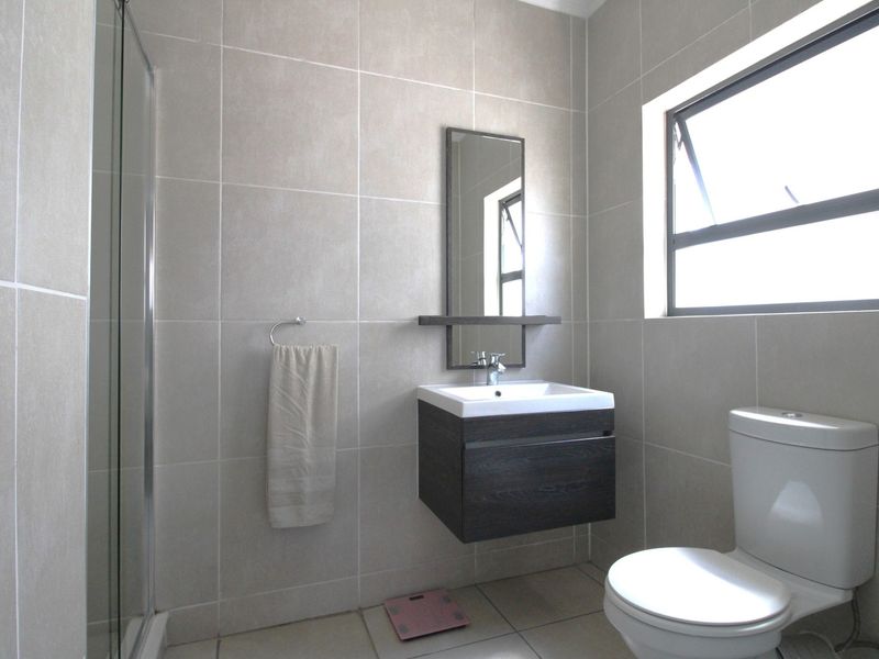 Modern bathroom featuring a wall-mounted vanity, glass shower enclosure, neutral floor-to-ceiling tiling, and a functional casement window for natural light.
