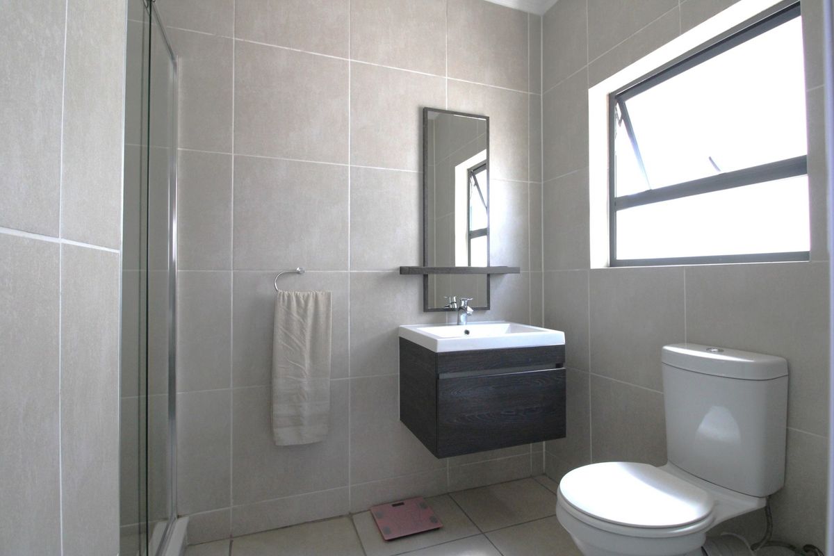 Modern bathroom featuring a wall-mounted vanity, glass shower enclosure, neutral floor-to-ceiling tiling, and a functional casement window for natural light.