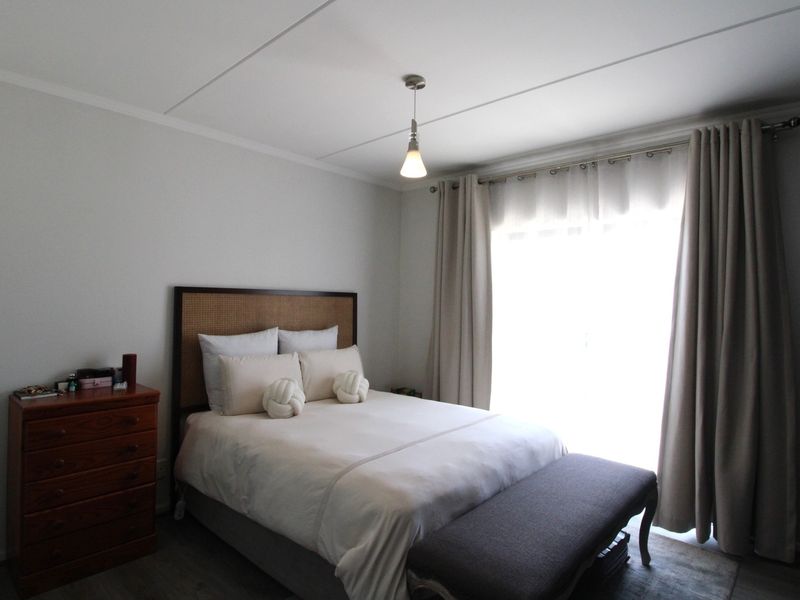 A well-maintained bedroom featuring neutral wall finishes, laminate flooring, and a large window with curtain tracks allowing for natural light.