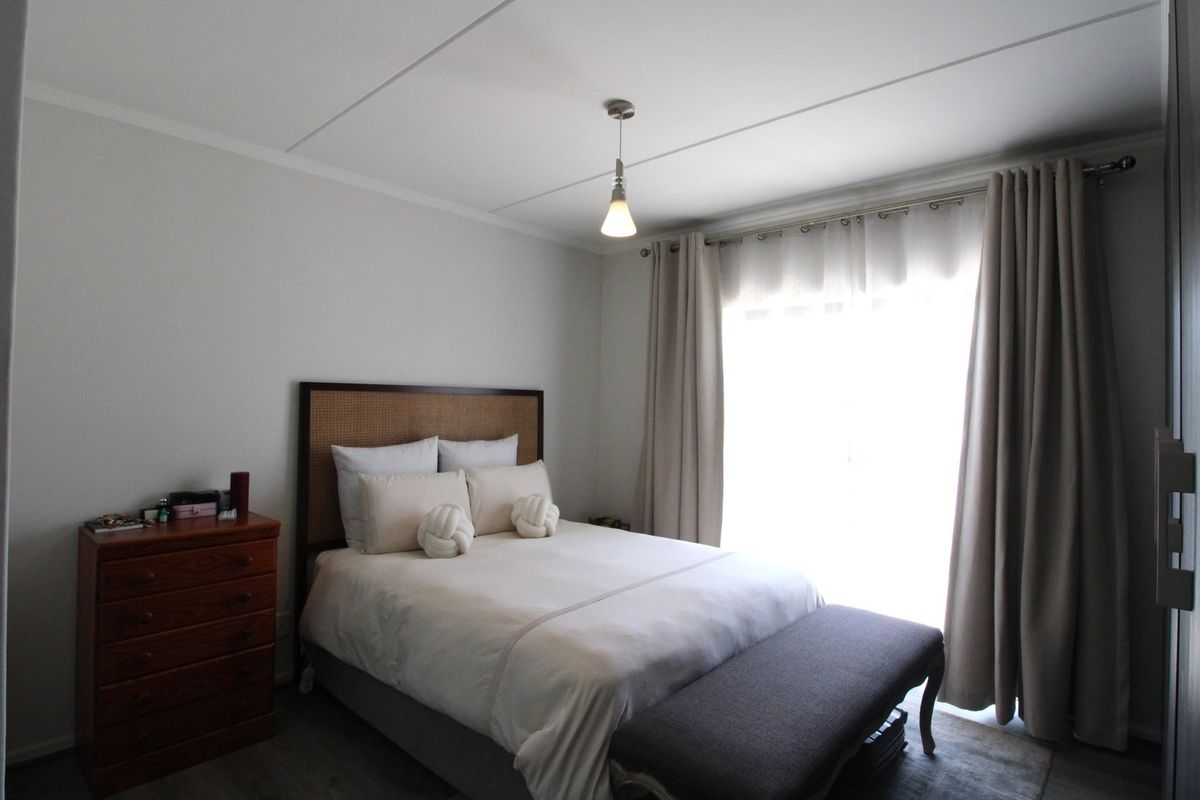 A well-maintained bedroom featuring neutral wall finishes, laminate flooring, and a large window with curtain tracks allowing for natural light.