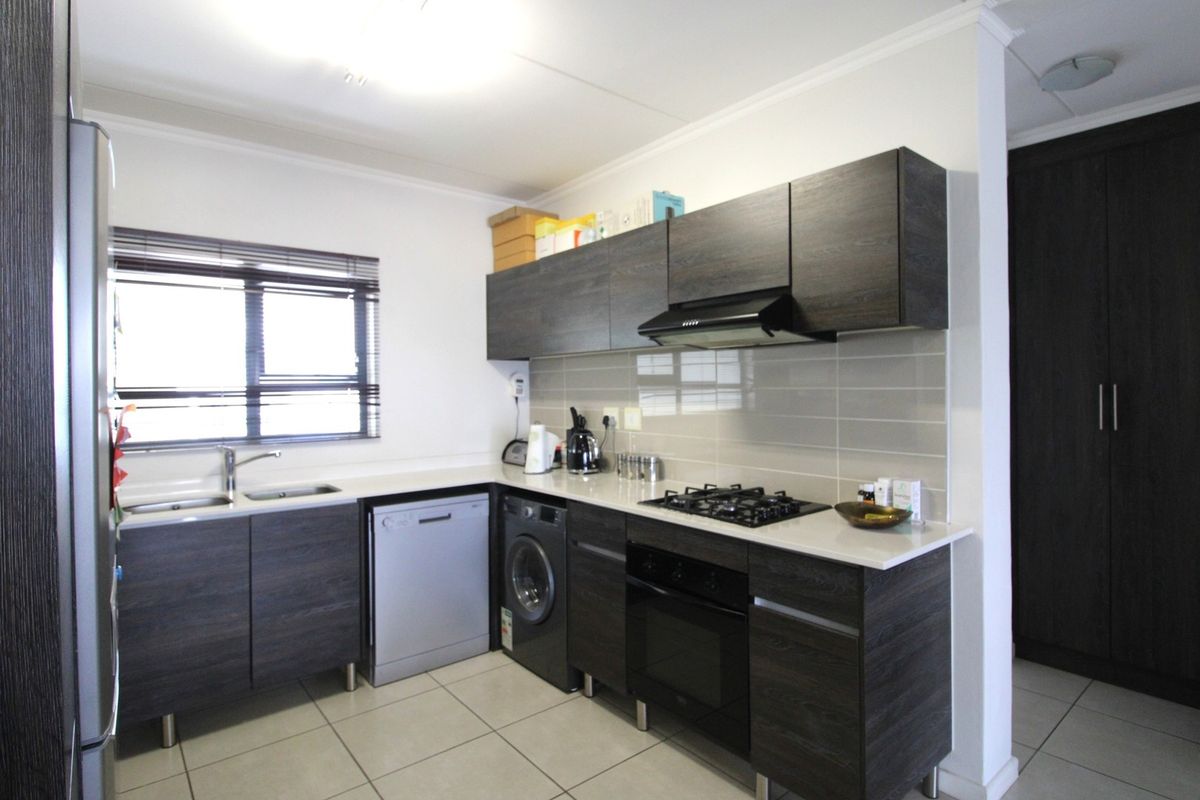 Modern kitchen featuring dark wood cabinetry, stone countertops, gas hob, electric oven, extractor fan, and tiled flooring with a neutral backsplash.