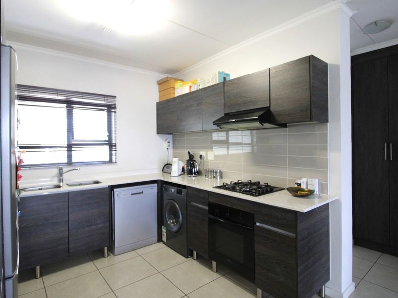Modern kitchen featuring dark wood cabinetry, stone countertops, gas hob, electric oven, extractor fan, and tiled flooring with a neutral backsplash.