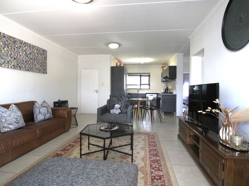 An open-plan living and kitchen area featuring tiled flooring, neutral walls, and a functional kitchen layout with built-in cabinetry.
