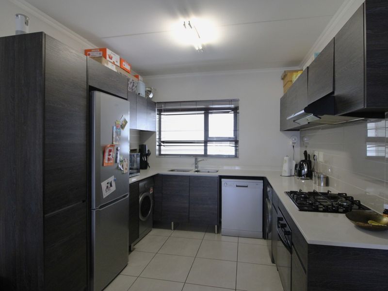 Modern kitchen featuring dark wood cabinetry, stone countertops, a gas hob, built-in oven, and tiled flooring with ample storage space.