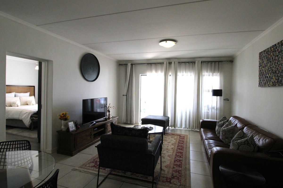 A well-maintained living room featuring tiled flooring, coved ceilings, and a sliding glass door providing natural light and access to the exterior.