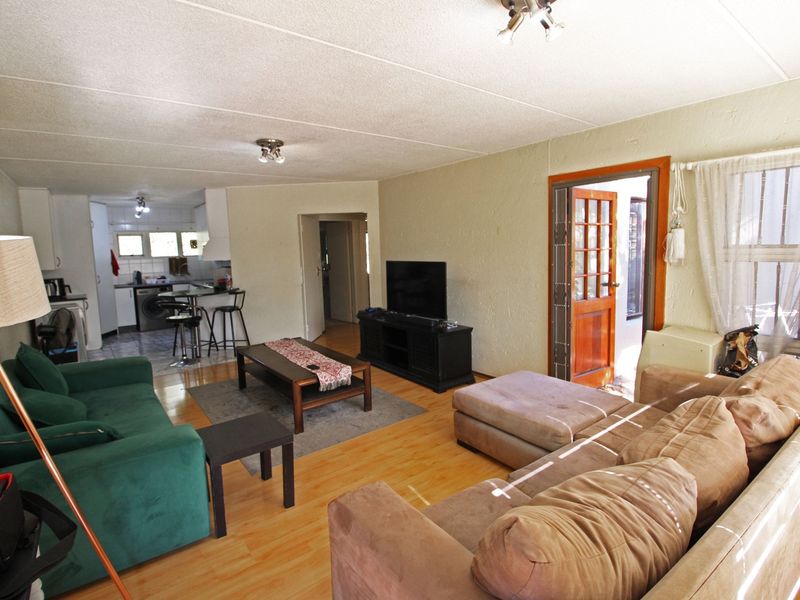 Open plan living area featuring laminate flooring, connected to a functional kitchen space with direct access to an outdoor area through a timber door.
