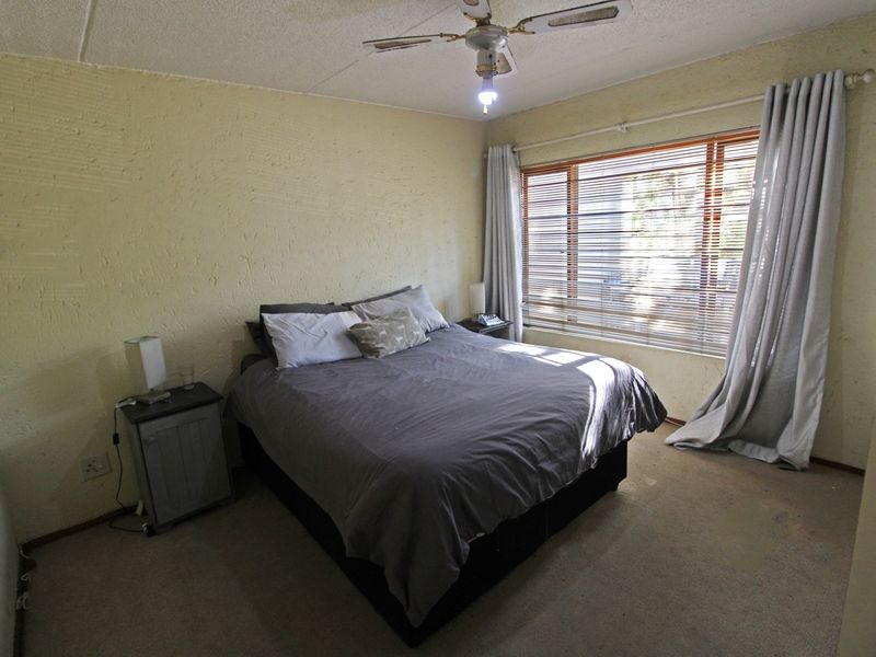 A bedroom featuring textured walls, carpet flooring, a ceiling fan, and large windows with venetian blinds.