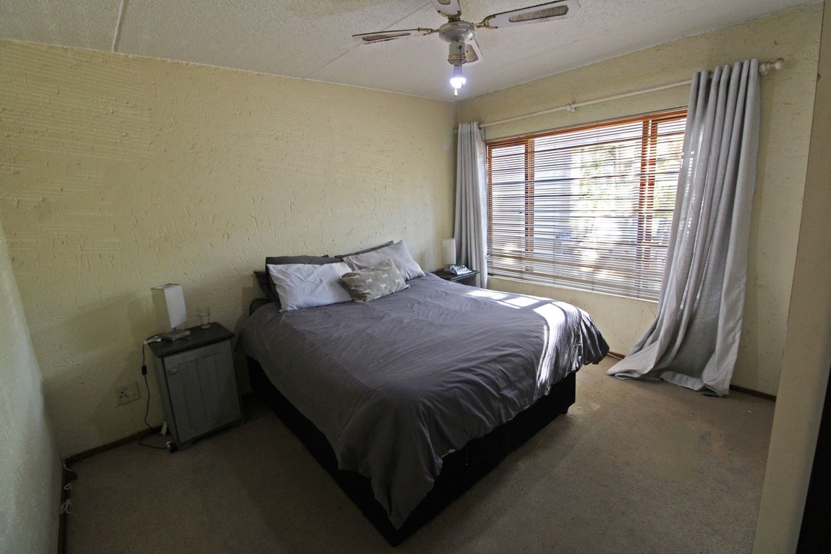 A bedroom featuring textured walls, carpet flooring, a ceiling fan, and large windows with venetian blinds.