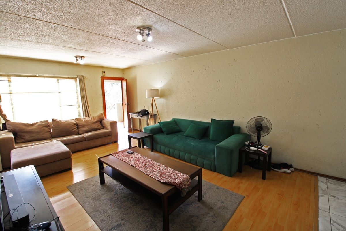 A spacious living room featuring laminate flooring, textured ceilings, and natural light from a large window, offering a functional layout for relaxation.