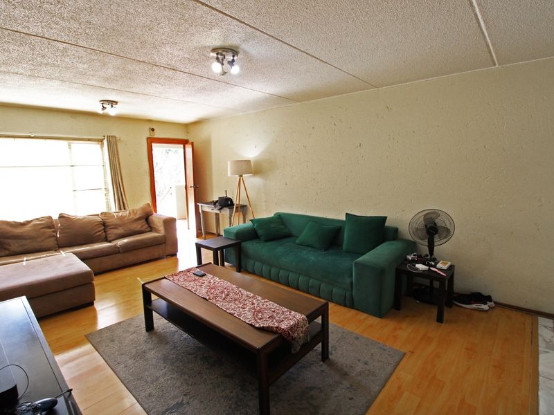 A spacious living room featuring laminate flooring, textured ceilings, and natural light from a large window, offering a functional layout for relaxation.