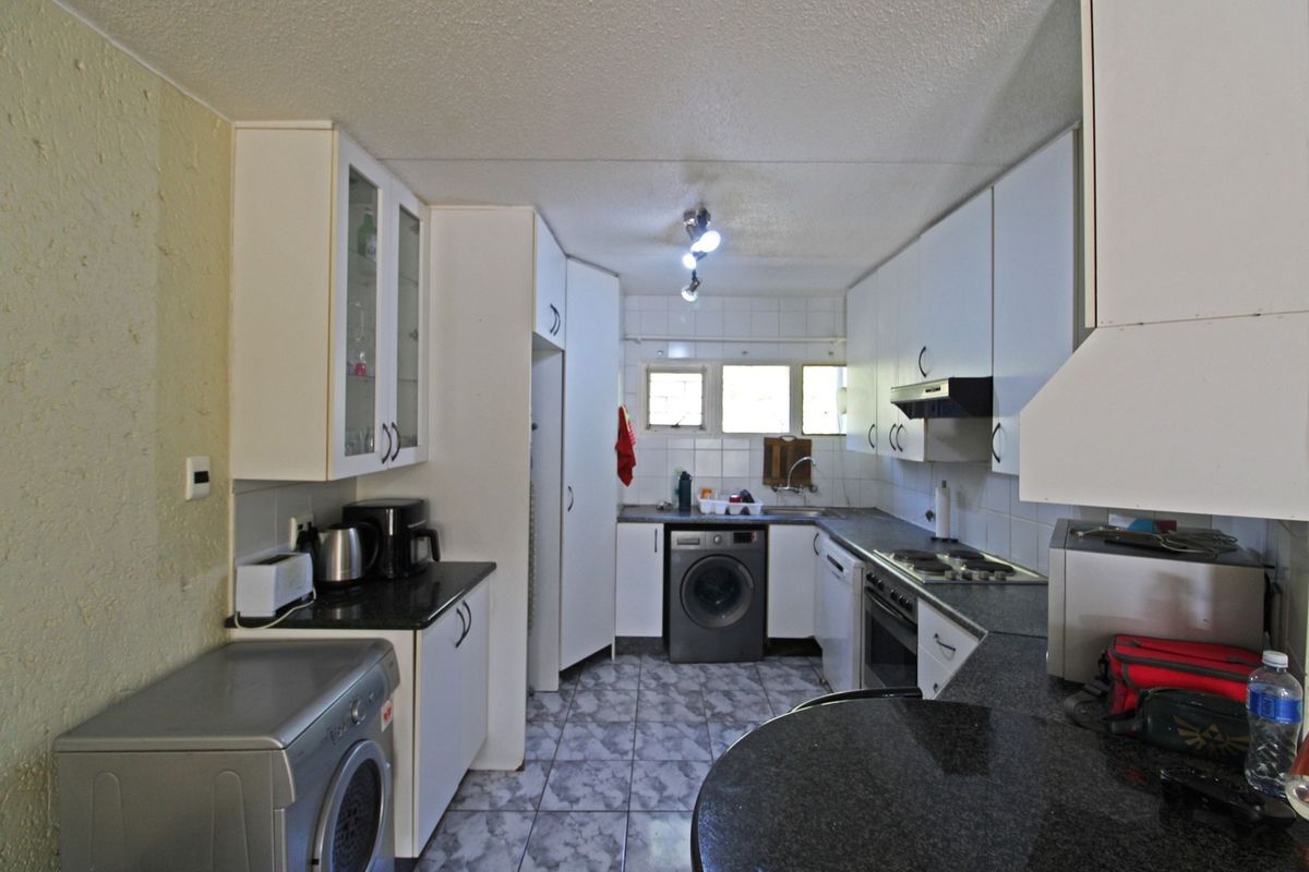 Functional kitchen featuring granite countertops, built-in cabinetry, integrated oven and hob, and tiled flooring, offering a practical layout for daily meal preparation.