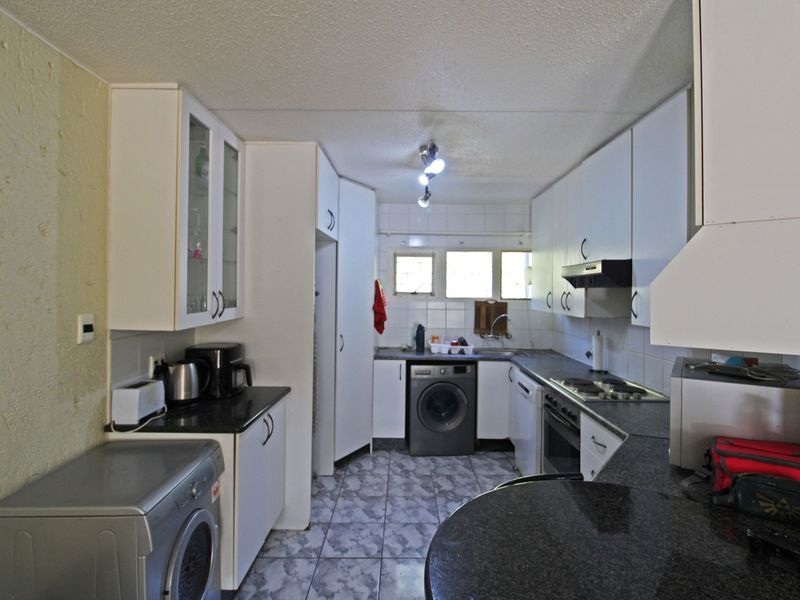 Functional kitchen featuring granite countertops, built-in cabinetry, integrated oven and hob, and tiled flooring, offering a practical layout for daily meal preparation.