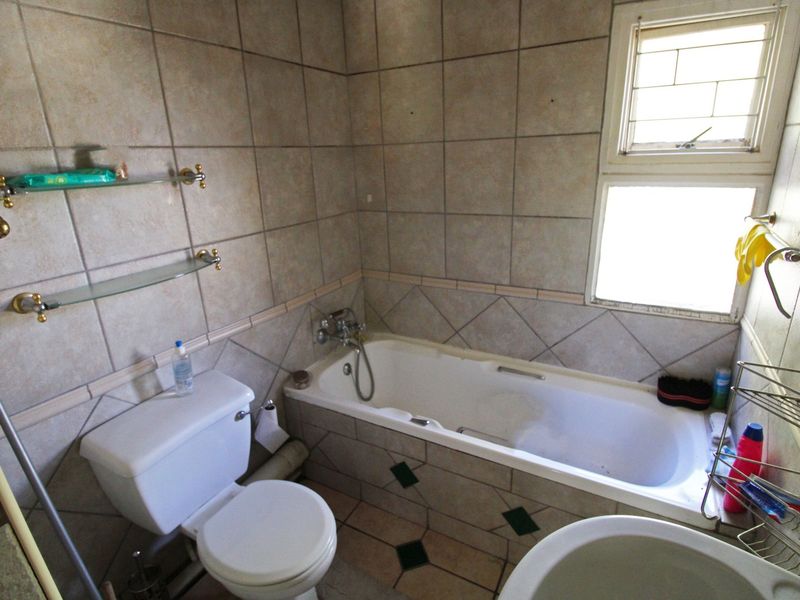 A dated bathroom featuring a bathtub, toilet, and basin with tiled walls and flooring, requiring cosmetic updates to modernize the space.