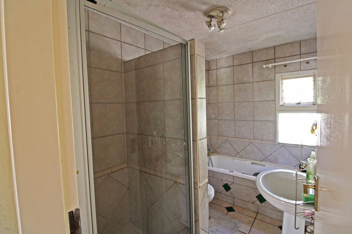 A dated bathroom featuring a shower enclosure, bathtub, and pedestal basin with tiled walls and flooring.