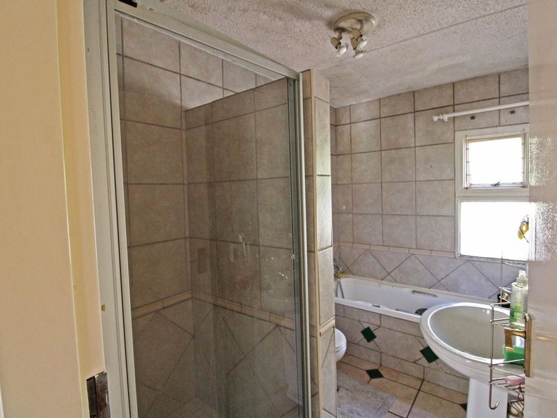 A dated bathroom featuring a shower enclosure, bathtub, and pedestal basin with tiled walls and flooring.