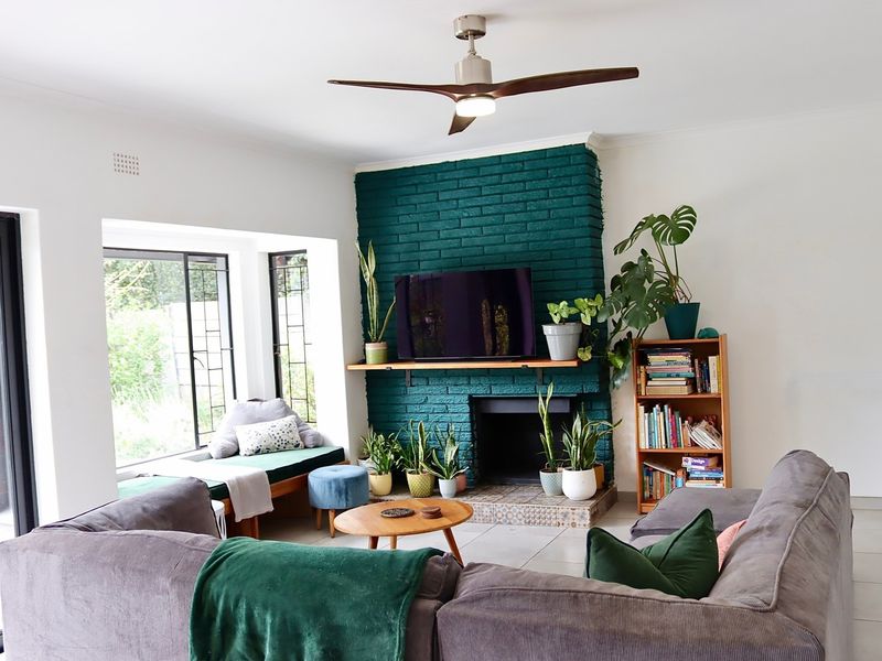 A comfortable living room featuring a striking green painted brick fireplace, a built-in window seat, and a modern ceiling fan.