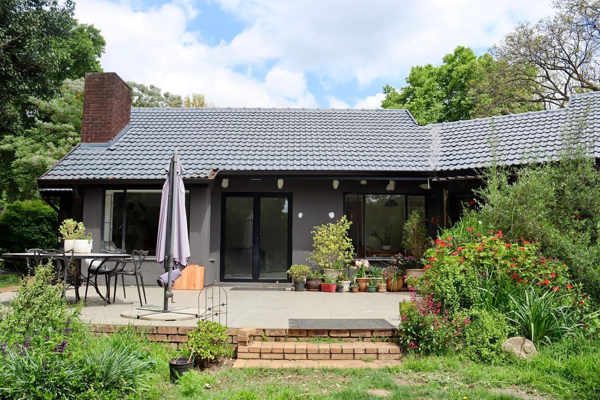 Rear view of the house featuring a tiled roof, brick chimney, and a paved patio area leading to the garden through double glass doors.