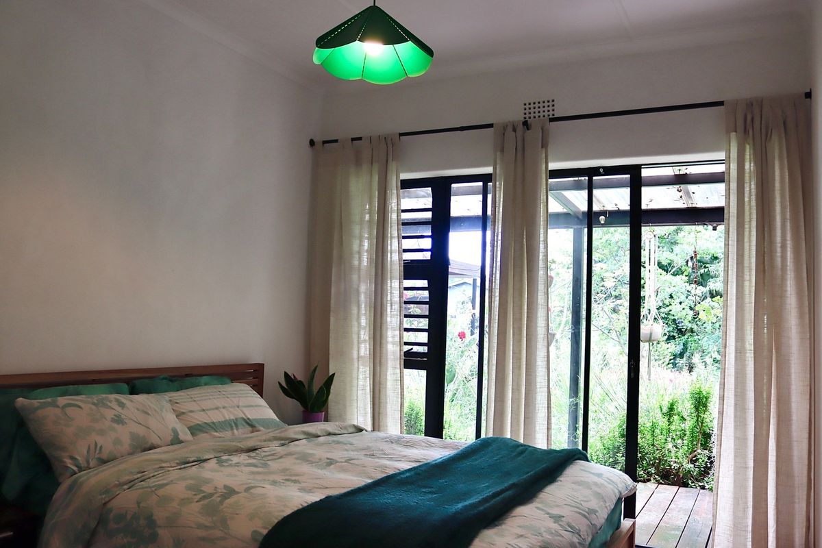 A bright bedroom featuring sliding glass doors that open onto a wooden deck and garden area.