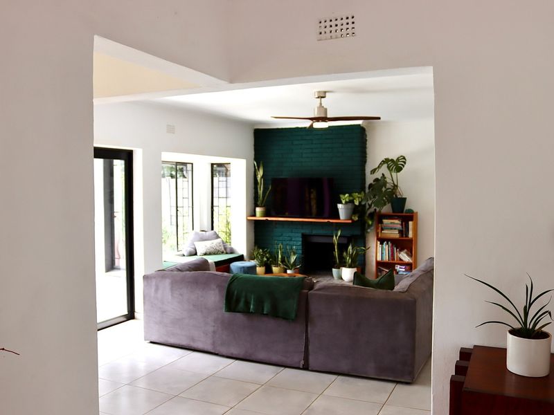 Spacious living room featuring a painted brick fireplace, ceiling fan, tiled flooring, and large sliding glass doors leading to the outdoor area.