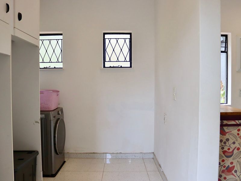A functional laundry area featuring tiled flooring, built-in cabinetry, and security-barred windows, providing a practical space for utility tasks.