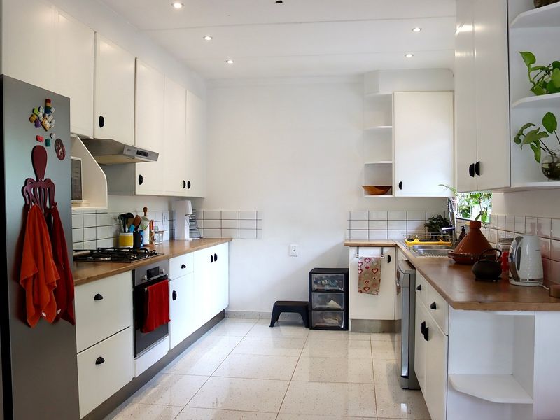 A functional galley-style kitchen featuring white cabinetry, wooden countertops, a gas hob, built-in oven, and tiled flooring with recessed lighting.