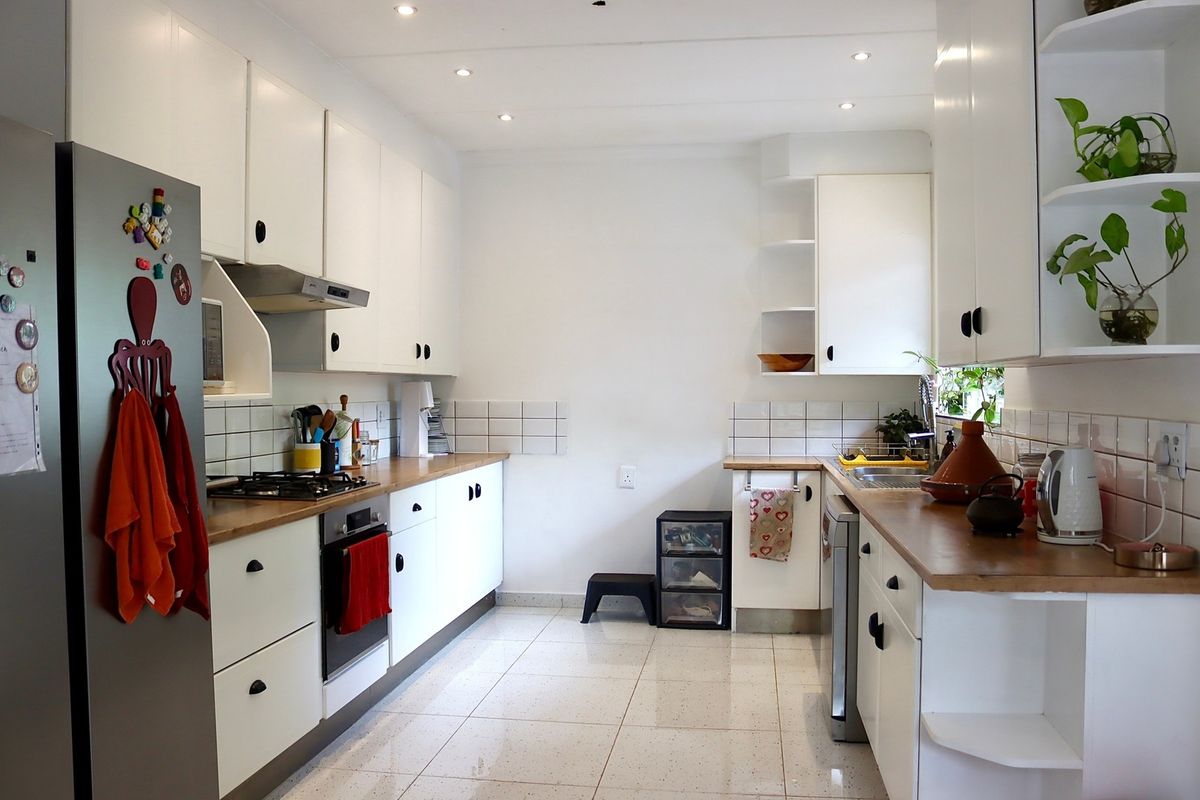 A functional galley-style kitchen featuring white cabinetry, wooden countertops, a gas hob, built-in oven, and tiled flooring with recessed lighting.