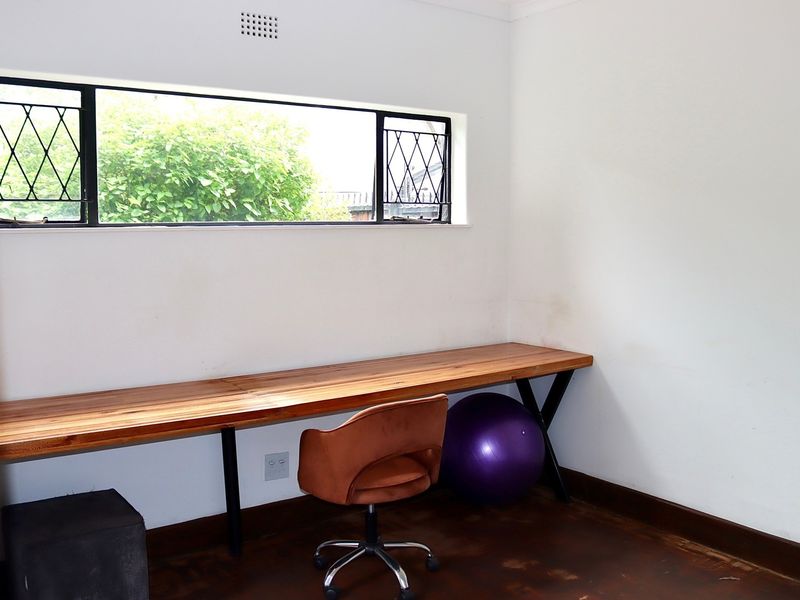 A functional home office space featuring a built-in wooden desk, leaded glass window, and dark timber flooring.