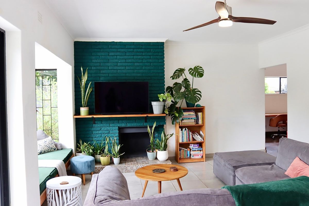 A comfortable living room featuring a striking green painted brick fireplace, tiled flooring, and a built-in window seat, complemented by a modern ceiling fan.