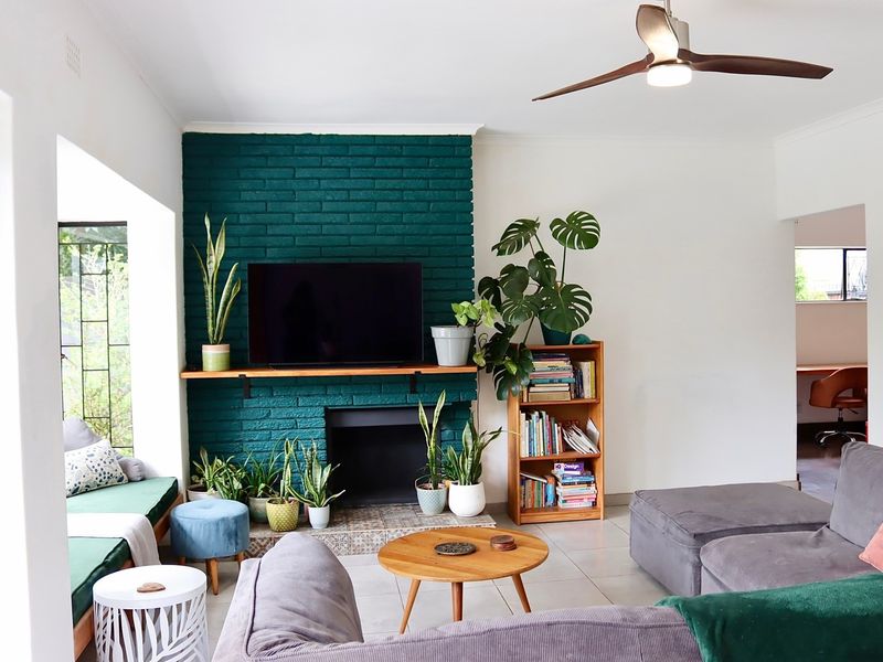 A comfortable living room featuring a striking green painted brick fireplace, tiled flooring, and a built-in window seat, complemented by a modern ceiling fan.