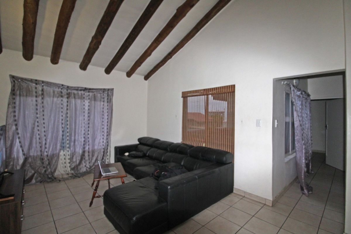 Living room featuring a vaulted ceiling with exposed timber beams and tiled flooring, providing a spacious and rustic atmosphere.